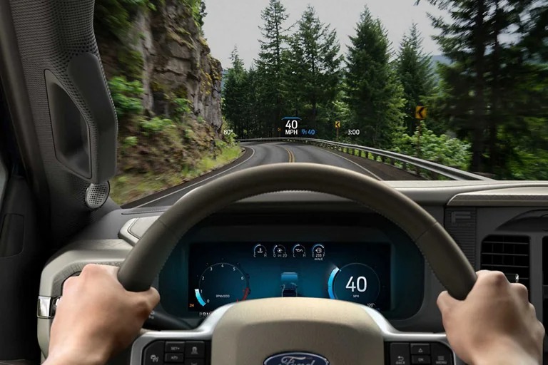 View from the driver's seat of a Ford vehicle on a winding road, showcasing the digital dashboard and heads-up display.